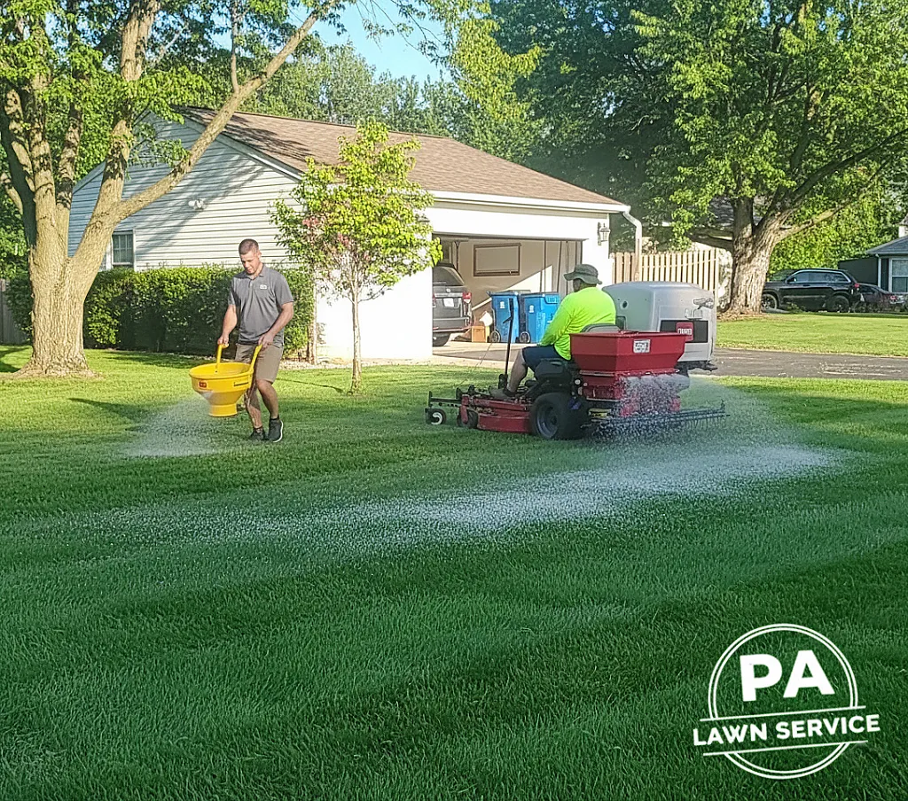 A professional applying granular fertilizer to a lush, green lawn in Hopkins, MN