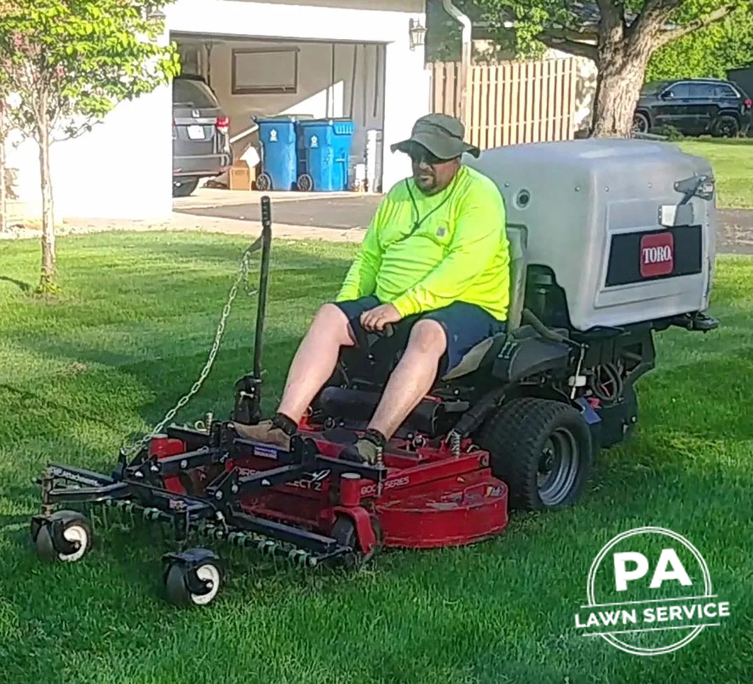 A professional landscaper using a leaf blower to clear leaves from a residential lawn.